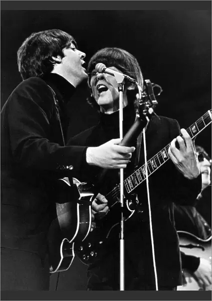Paul McCartney and George Harrison share a microphone on stage