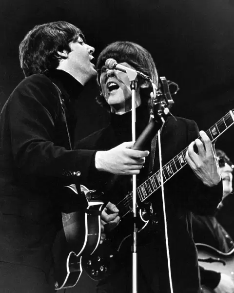Paul McCartney and George Harrison share a microphone on stage