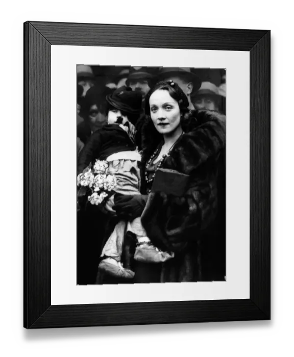 Framed Print : Marlene Dietrich (1931). The film actress famed for her performance in The Blue Angel'photographed with a child dressed as Charlie Chaplin on her arrival at Liverpool Street Station