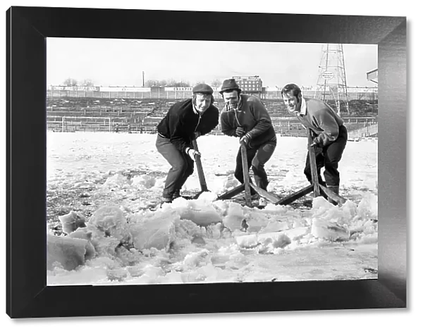 Bolton Wanderers players clear the snow from the pitch at Burnden Park