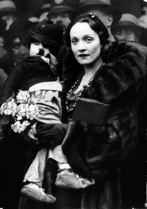 Framed Print : Marlene Dietrich (1931). The film actress famed for her performance in The Blue Angel'photographed with a child dressed as Charlie Chaplin on her arrival at Liverpool Street Station