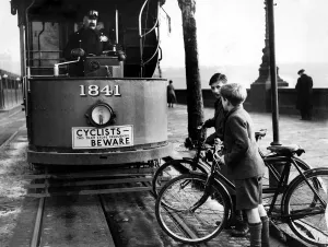 Children on bicycles crossing in front of a tram
